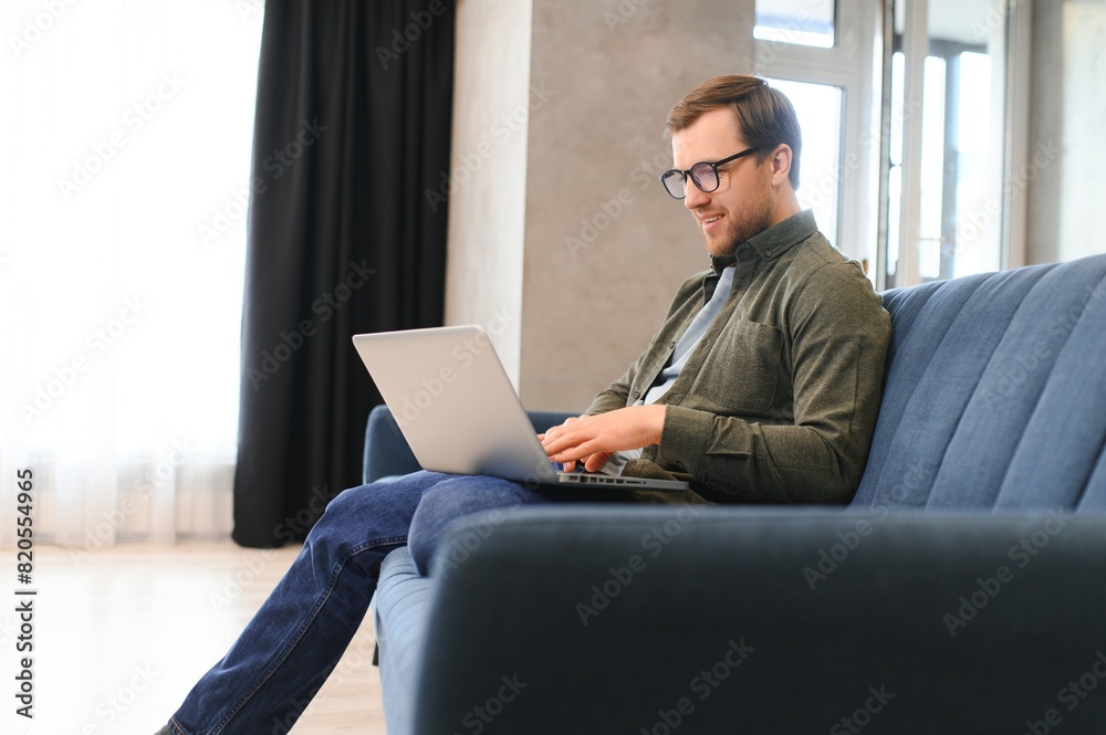 Young cheerful man sitting on sofa with laptop Young cheerful man sitting on sofa with laptop