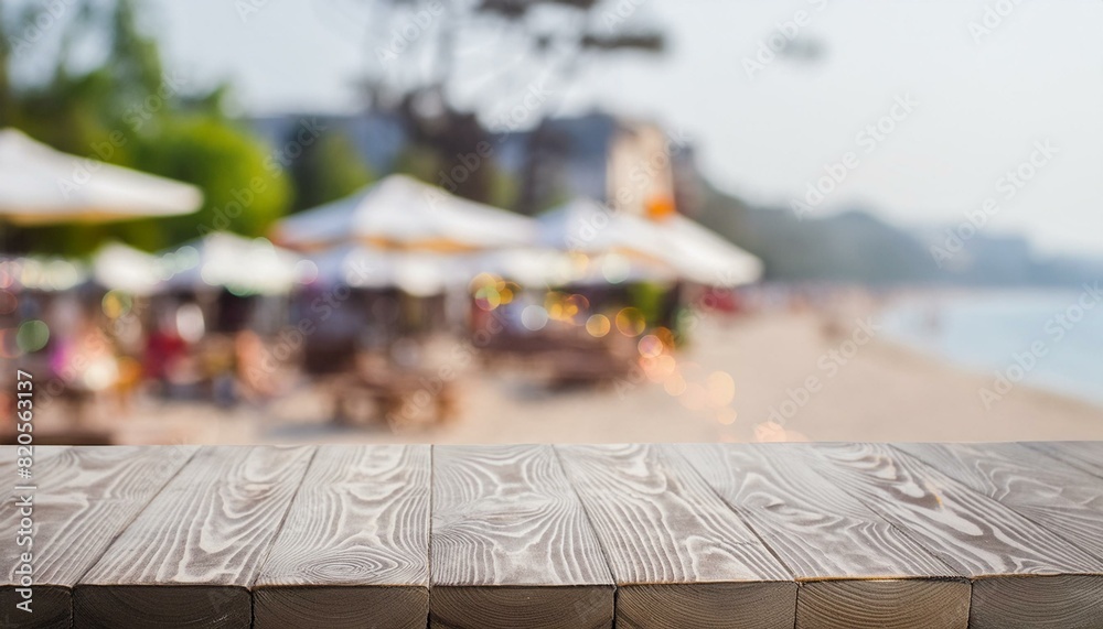 Naklejka premium Breezy Evenings: Wooden Table with Bokeh Beach Café Background