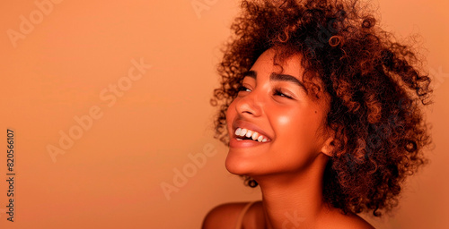 Happy woman with curly hair laughing against a peach background with copy space