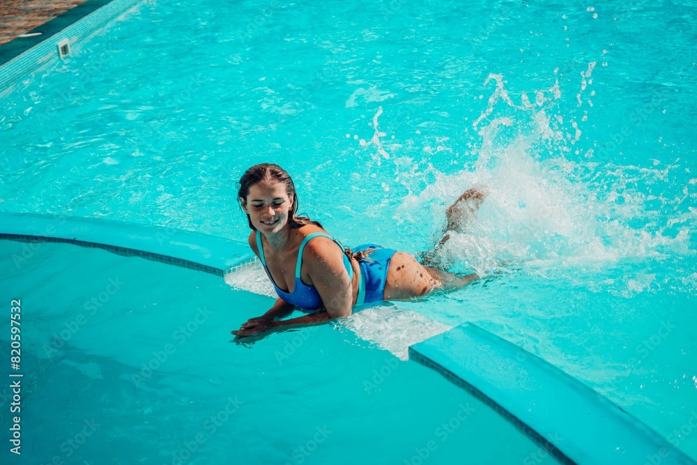 A woman is in the water, smiling and enjoying herself. The water is blue and the pool is surrounded by a white ledge.