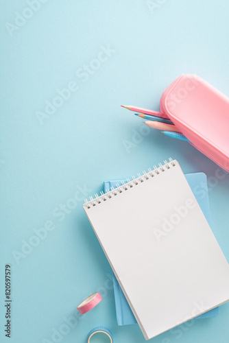 A vertical neatly organized blue workspace featuring a blank notepad, pink pencil case with colored pencils, and washi tape © ActionGP