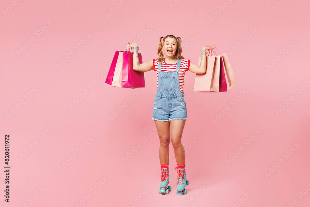 Full body young happy woman wear red t-shirt denim overalls casual clothes rollers rollerblading hold package bags after shopping isolated on plain pink background. Summer sport, sale buy day concept. Full body young happy woman wear red t-shirt denim overalls casual clothes rollers rollerblading hold package bags after shopping isolated on plain pink background. Summer sport, sale buy day concept.