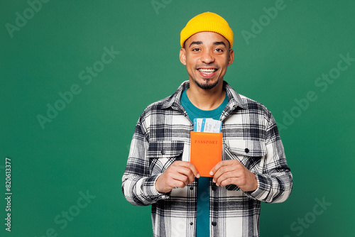 Traveler smiling fun man wear shirt hat hold passport boarding ticket isolated on plain green background studio. Tourist travel abroad in free spare time rest getaway. Air flight trip journey concept.