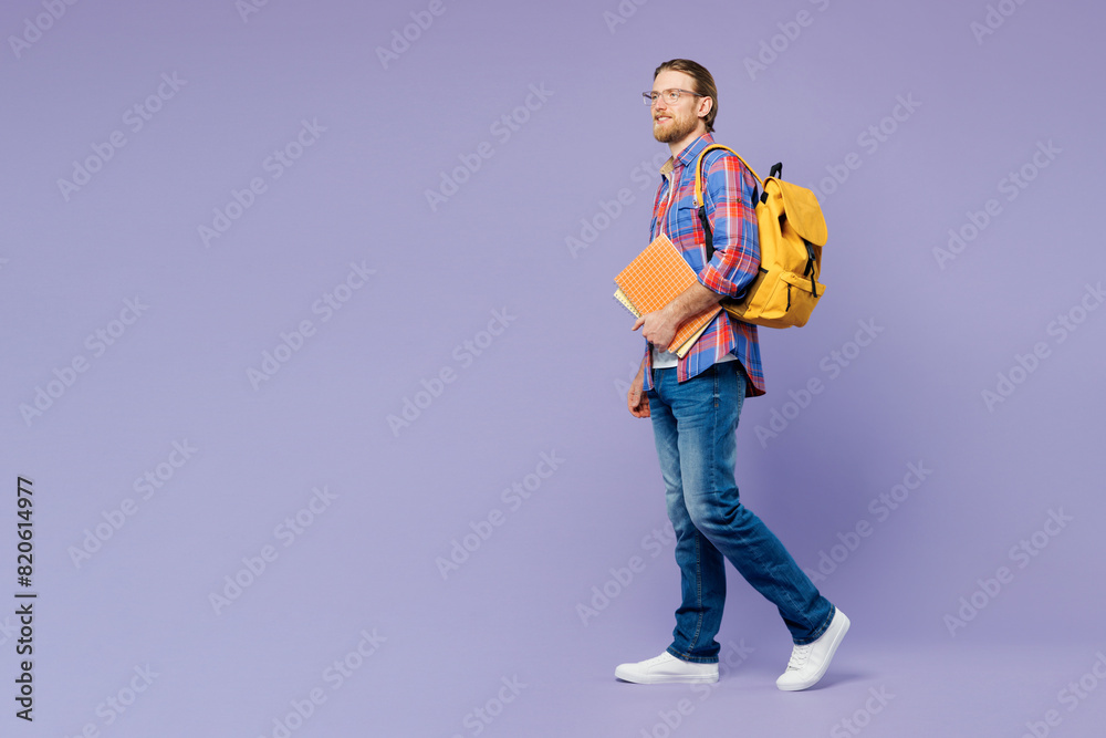 Full body side view young happy cheerful smart boy student wears blue casual clothes backpack bag hold books walk go isolated on plain pastel purple background. High school university college concept. Full body side view young happy cheerful smart boy student wears blue casual clothes backpack bag hold books walk go isolated on plain pastel purple background. High school university college concept.