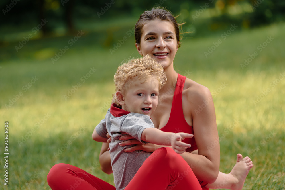 Young happy sporty woman doing exercises together with her cute kid in park, Outdoor yoga bonding: A young woman and her child stretch together, embracing family warmth