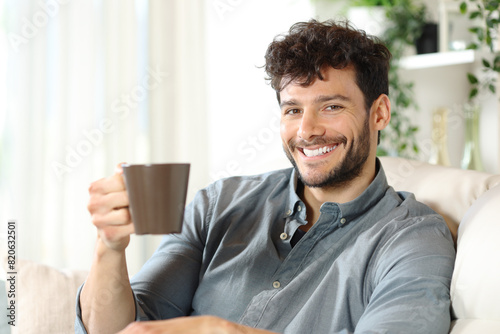 Happy man drinking coffee at home looking at camera
