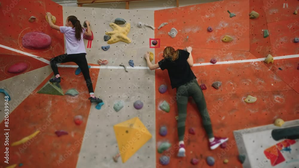 Two small strong and brave girls of 14 and 10 years old are training on the wall of a climbing wall indoors. Adults and younger children train together. The girls support each other in sports. 4k