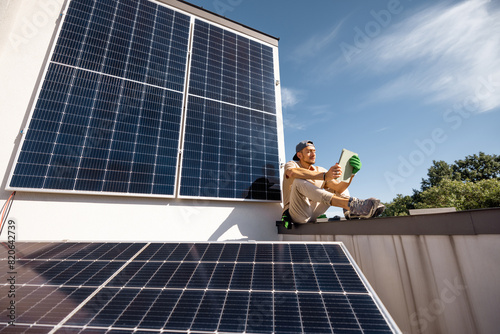Man sitting on a rooftop and using digital tablet monitoring production from the solar power station installed on his property. Concept of modern technologies and sustainable lifestyle