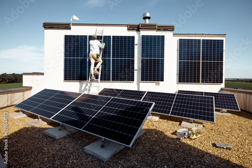 Man installing solar panels, climbing on a ladder on the roof of his house. Wide angle view on a roof with solar power station. Renewable energy and sustainability concept