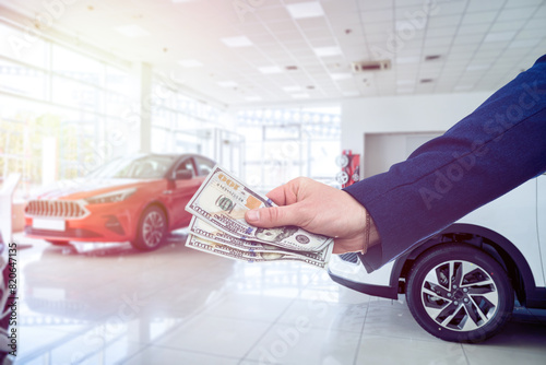 business man gives dollar cash when buying a car at showroom. Concept of purchase or rent vechicle photo