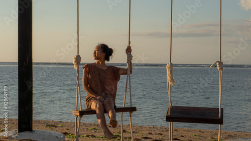 A woman is seen from behind, swinging over the ocean as the sunsets on the beach.