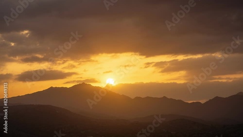 4k uhd dramatic sunset cloudy sky timelapse - Sun sets among clouds infiltrating through them with its rays then disappears among the mountains with the dark sky turning reddish