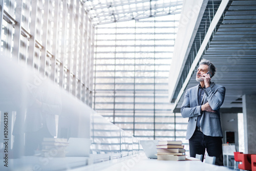 Handsome businessman working on laptop, searching for informations in book and making phone call. Traditional information source in modern office space. photo