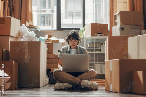 A young person sitting cross-legged on the floor, using a laptop, surrounded by moving boxes in a room. A moving or unpacking process. AI generative photo
