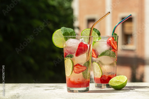 Refreshing summer cocktail with strawberries, lime, mint leaves, ice cubes. Strawberry mojito. Cold fresh drink  in a glass, green outdoor  on background, hard light.
