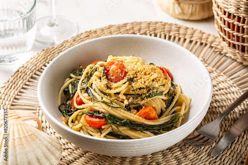 Spaghetti with agretti, or salsola soda, tomatoes, bread crumbs, pinoli pine nuts and anchovy in a white plate. Italian pasta, white dinner table.