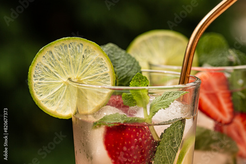 Close up of slice of lime on a Strawberry mojito glas. Cold fresh drink, green outdoor on background. Refreshing summer cocktail with strawberries, lime, mint leaves, ice cubes.