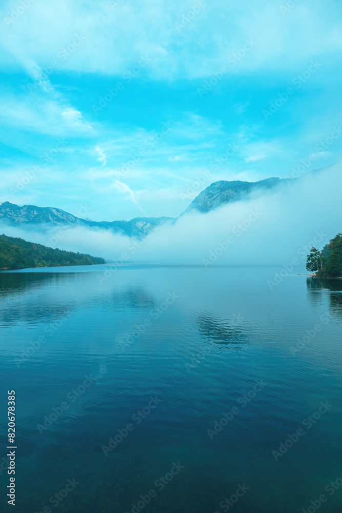 Morning fog and mist rising from the surface of Lake Bohinj in summer sunrise