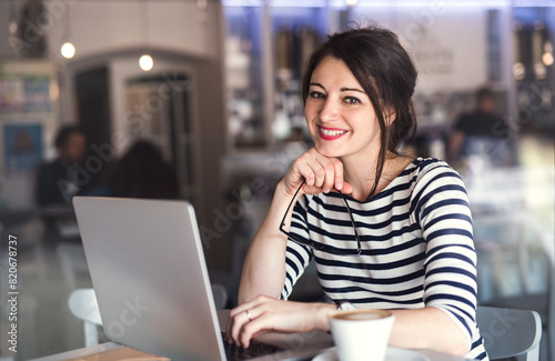 Woman working remotely from coffee shop. Cappucino and laptop on table. Female freelancer working on notebook in cafe. Free Download Woman working remotely from coffee shop. Cappucino and laptop on table. Female freelancer working on notebook in cafe. - GFXLoad