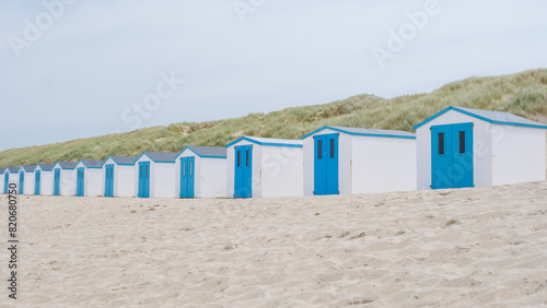 A charming row of beach huts with vibrant blue doors standing on the sandy shores of Texel, creating a picturesque scene against the backdrop of the sea.