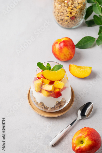 Flat lay of greek yogurt parfait with peach and muesli in a glass on a light background with fresh fruits and spoon. Healthy eating concept.