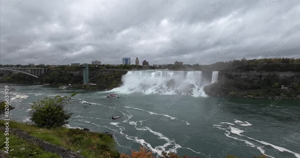 Niagara Falls from the Canadian side overlooking the waterfalls on the American side on a cloudy day with boats sailing over the water in front of the waterfall. Niagara Falls from the Canadian side overlooking the waterfalls on the American side on a cloudy day with boats sailing over the water in front of the waterfall.