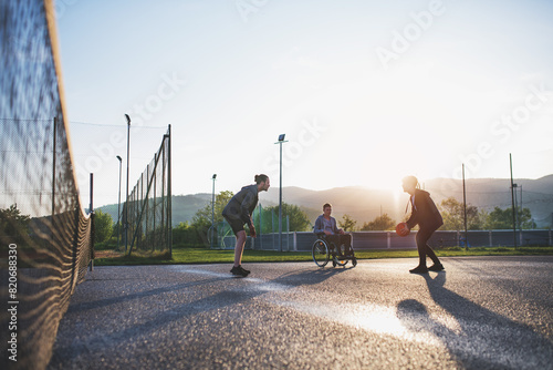 Disabled young man in a wheelchair playing basketball with his friends. Teamwrok and male friendship. photo