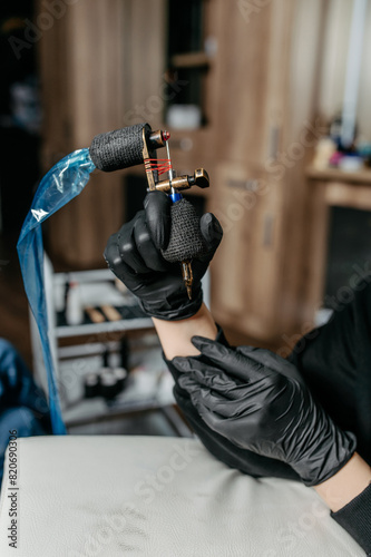  Woman professional tattoo artist in black gloves holding  a tattoo machine.