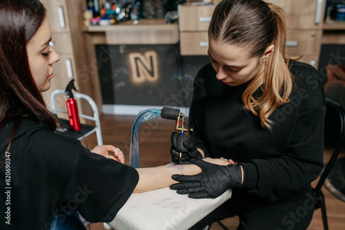 Woman professional tattoo artist in black gloves making a tattoo on a woman's forearm.