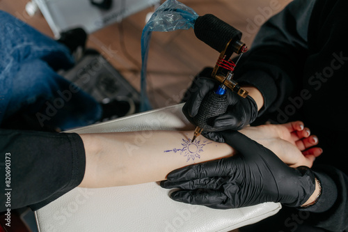 professional tattoo artist making a tattoo with a tattoo machine on a woman's forearm.