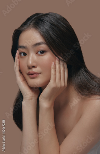 Close up vertical portrait, Attractive korean asian ethnicity woman holding hands near her face, posing over beige background.