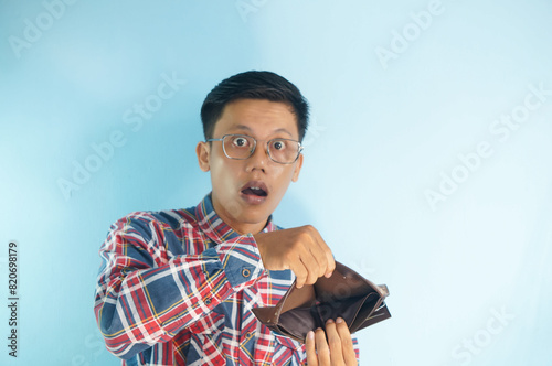 Young Asian man showing his empty wallet with worried expression