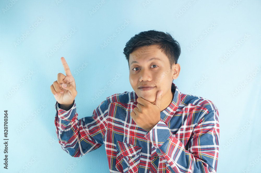 Handsome Asian man in red shirt is pointing his finger to the up at an empty space. showing option, recommendation, presentation Handsome Asian man in red shirt is pointing his finger to the up at an empty space. showing option, recommendation, presentation