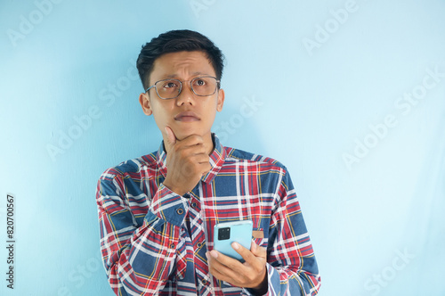 Young Asian man thinking about something while holding mobile phone photo