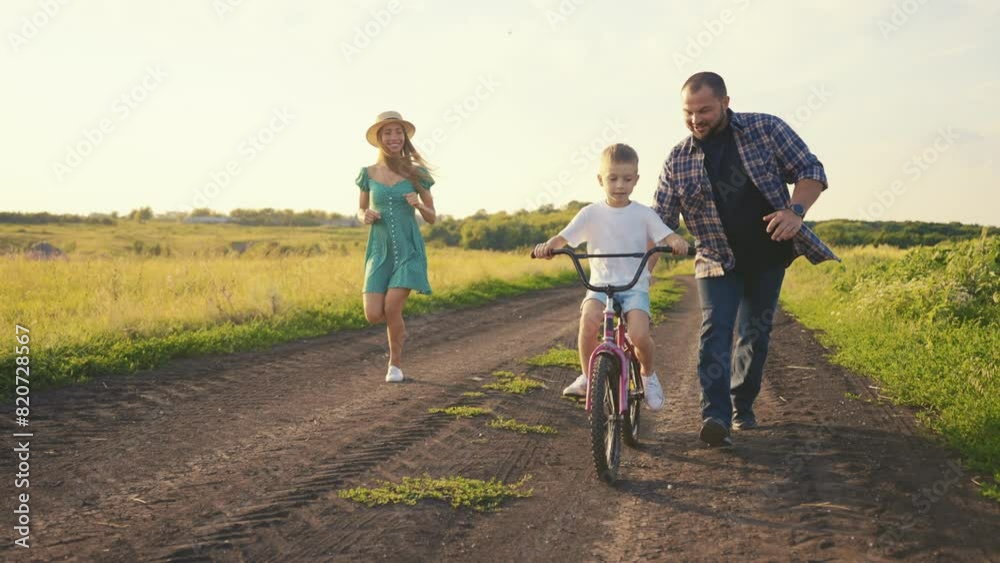 Childhood bike concept. Mother and dad teaching son to ride bicycle. Young family teaching son to ride bike first time on countryside rural road at sunset. Happy kid concept. The best moments together Childhood bike concept. Mother and dad teaching son to ride bicycle. Young family teaching son to ride bike first time on countryside rural road at sunset. Happy kid concept. The best moments together