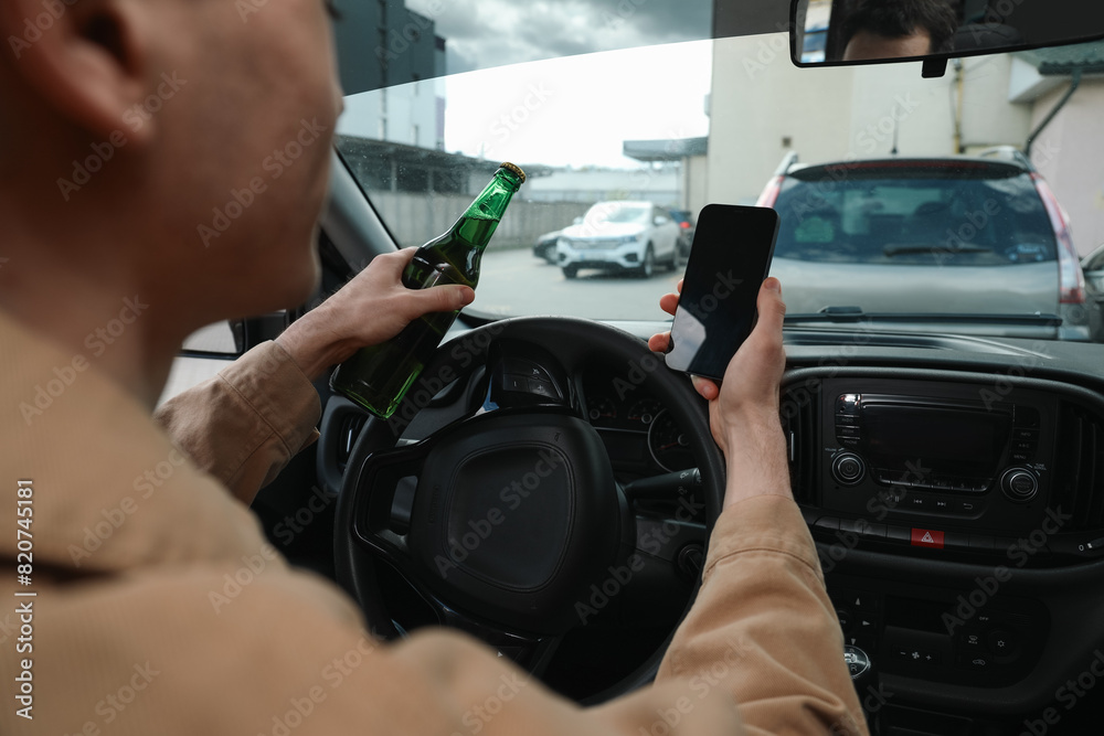 Man with bottle of beer and smartphone in car, closeup. Don't drink and drive concept Man with bottle of beer and smartphone in car, closeup. Don't drink and drive concept