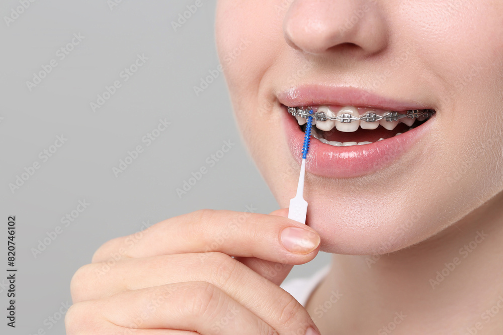 Obraz premium Smiling woman with dental braces cleaning teeth using interdental brush on grey background, closeup. Space for text
