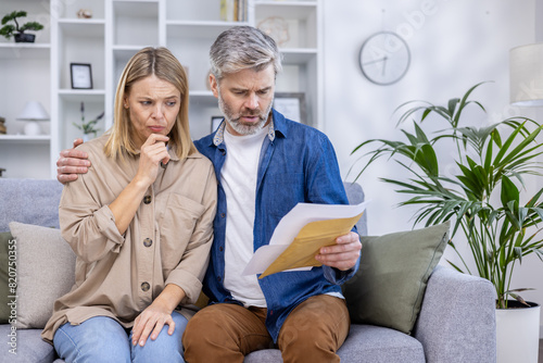 Fotografie A concerned couple sitting on the couch, examining financial paperwork in their living room