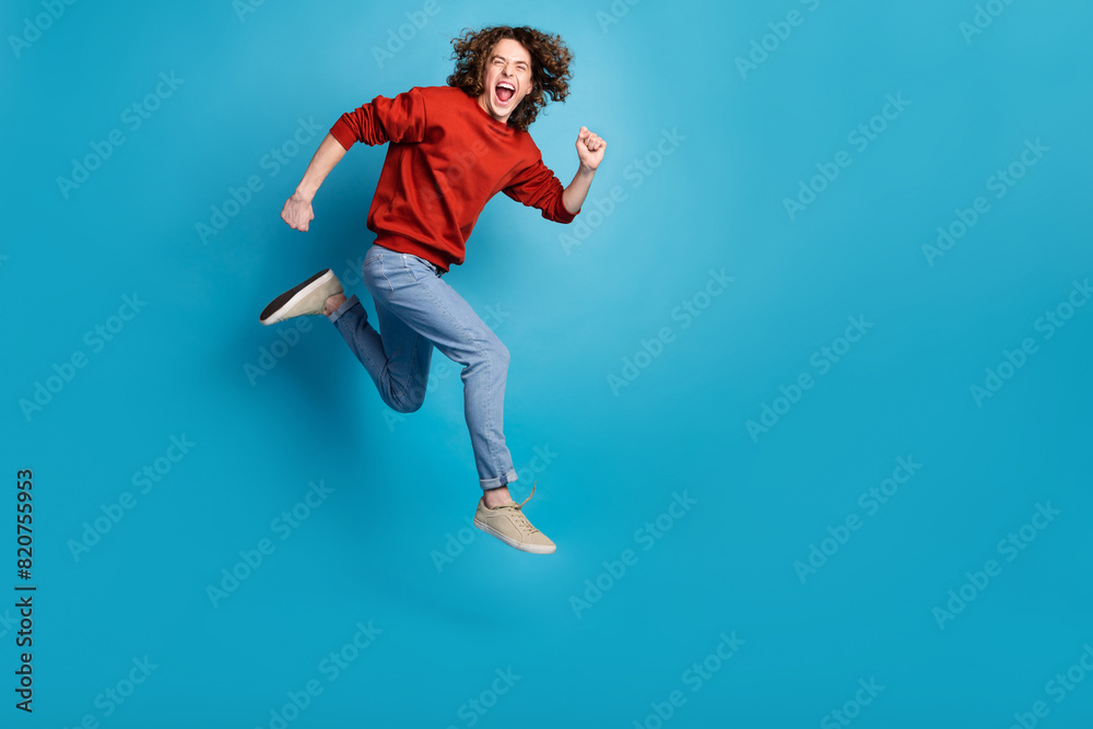 Full length photo of funny excited guy wear red sweater jumping high running emtpy space isolated blue color background