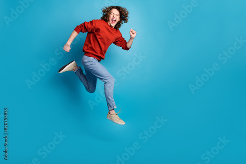 Full length photo of funny excited guy wear red sweater jumping high running emtpy space isolated blue color background © deagreez
