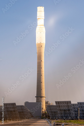 A dramatic image of a concentrated solar power plant tower with the sun's reflection under a clear sky during sunrise or sunset photo