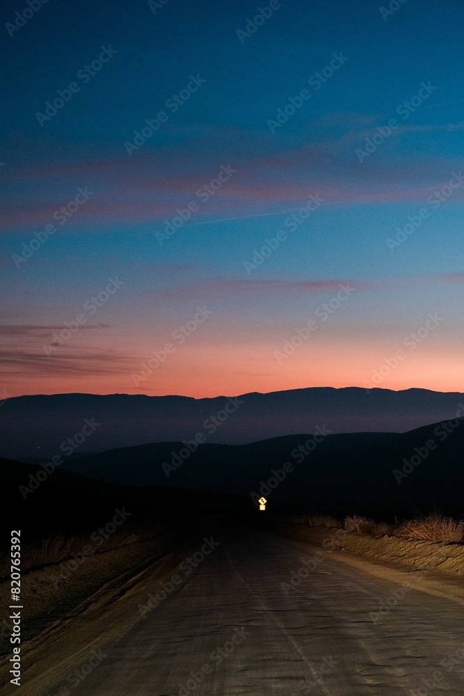 Fototapeta premium Dirt road with a mountain range in the background at sunset.
