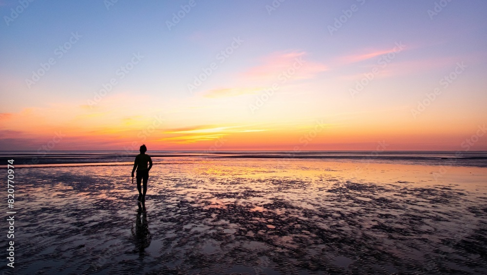 Young person stands on a serene tropical beach with a golden sunset in the background Young person stands on a serene tropical beach with a golden sunset in the background