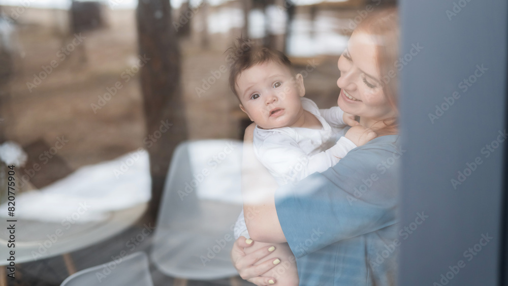 View through the window of a red-haired Caucasian woman holding her little son. 