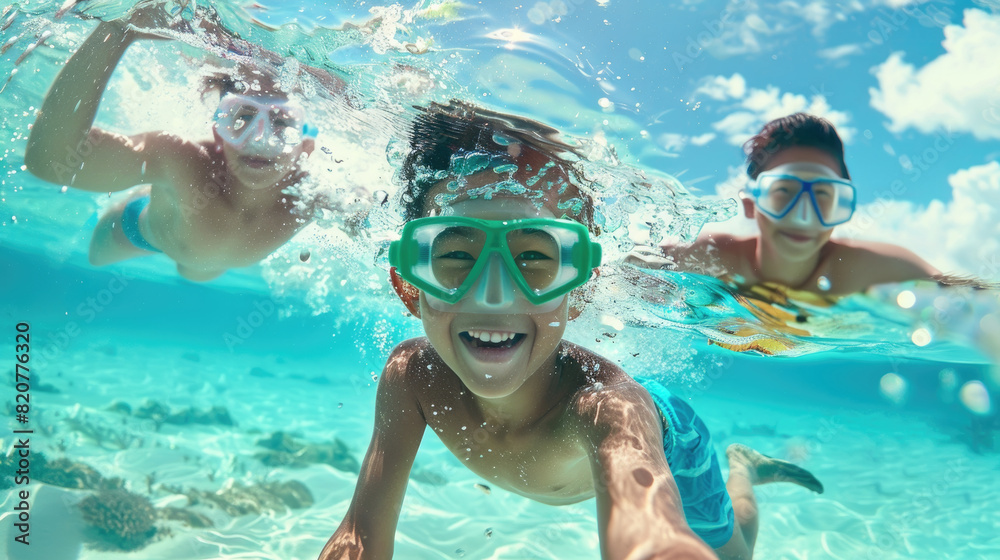 Fototapeta premium Three smiling children are snorkeling in clear blue tropical waters, exploring underwater marine life on a sunny day. They wear colorful snorkel masks and swim towards the camera with excitement