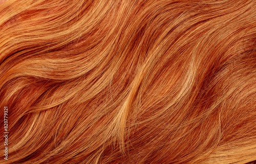 Red hair close-up as a background. Women's long orange hair. Beautifully styled wavy shiny curls. Hair coloring bright shades. Hairdressing procedures, extension.