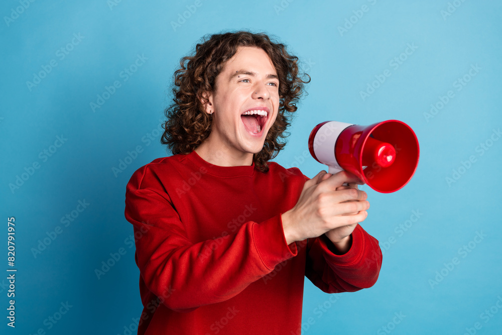 Photo of attractive funny guy wear red sweater yelling lous speaker emtpy space isolated blue color background