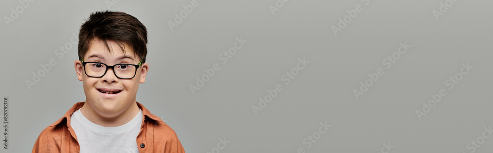 Cheerful boy with Down syndrome smiling in front of gray backdrop.