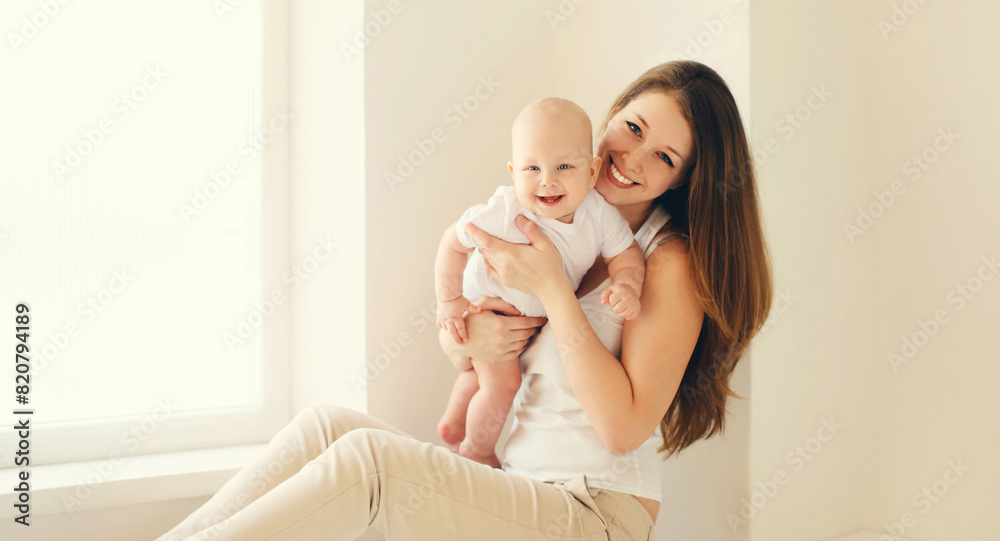 Happy smiling young mother playing with baby in white room at home Happy smiling young mother playing with baby in white room at home