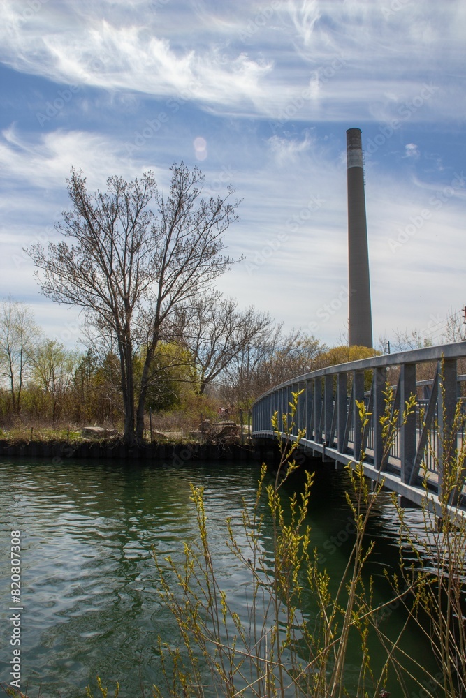Tranquil river with a bridge crossing over it with trees and industrial building in the background Tranquil river with a bridge crossing over it with trees and industrial building in the background